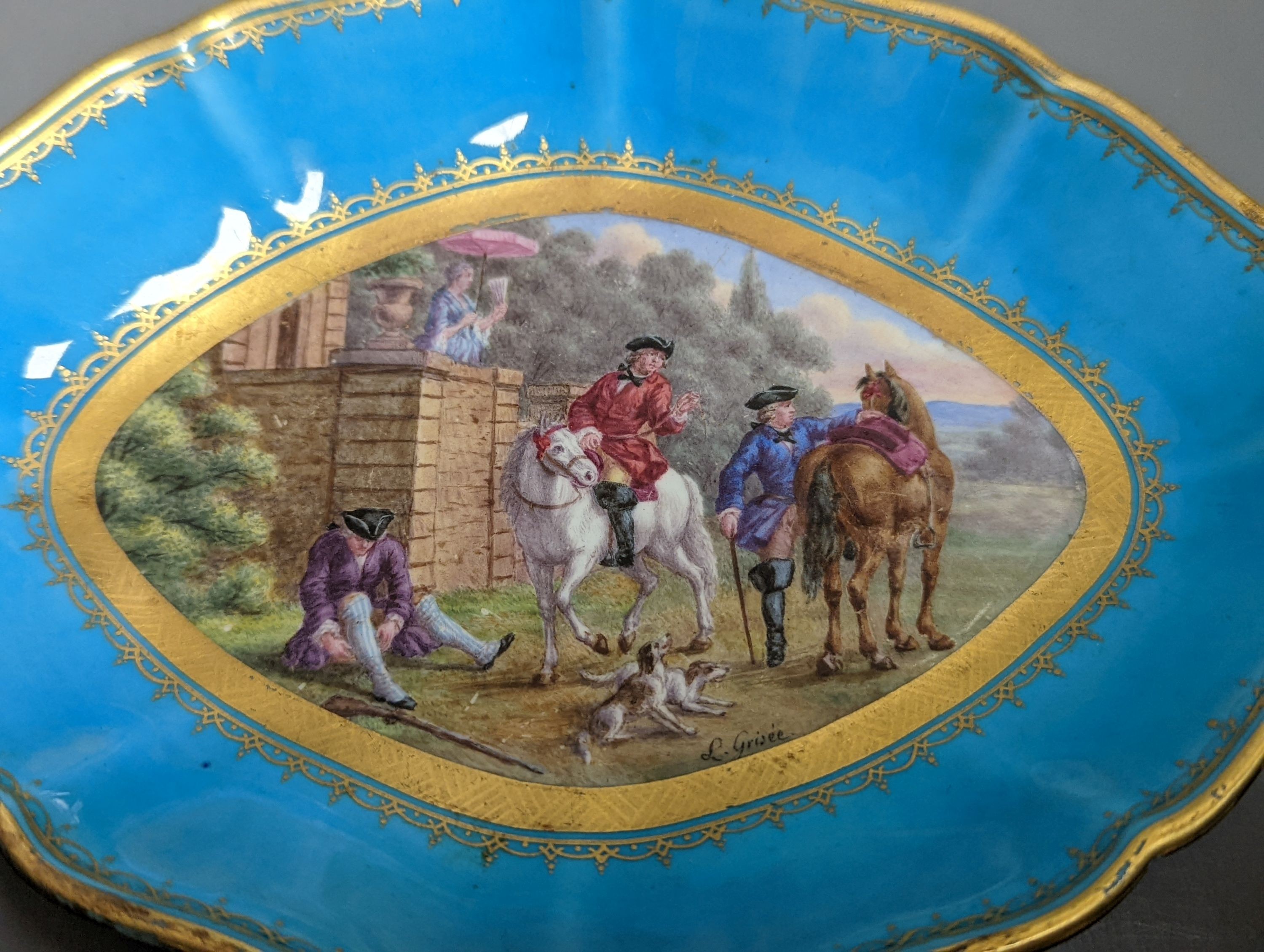 A 19th century Sevres oval shaped dish painted with a hunt scene, with three gentlemen, two dogs two horse and a lady watching surrounded by a turquoise and gilt ground, signed L Grise'e, 19cms wide